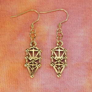 May include: A pair of gold dangle earrings featuring a tree of life design. The earrings are made of metal and have a delicate, intricate design.