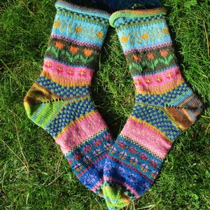 Könnte beinhalten: Ein Paar handgestrickte Socken mit einem lebendigen, mehrfarbigen Fair-Isle-Muster. Das Design umfasst horizontale Streifen in Blau, Pink, Grün und Orange mit komplizierten Blumen- und geometrischen Motiven im gesamten Gewebe der Socken.
