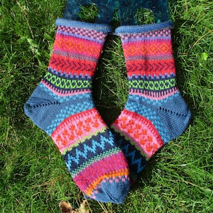 Könnte beinhalten: Ein Paar handgestrickte Socken mit einem lebendigen, mehrfarbigen Fair-Isle-Muster. Das Design umfasst horizontale Bänder aus blauen, rosa, orangefarbenen und grünen geometrischen Formen, mit einem einfarbig blauen Fersen- und Zehenbereich.