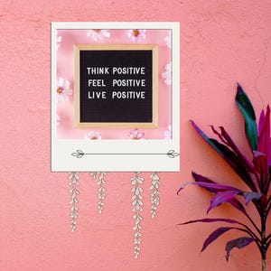 Może przedstawiać: Różowa ściana z białą ramą, w której znajduje się czarna tablica z literami z tekstem "Think Positive Feel Positive Live Positive". Tablica z literami jest otoczona białymi kwiatami. Po prawej stronie obrazu znajduje się fioletowa roślina.