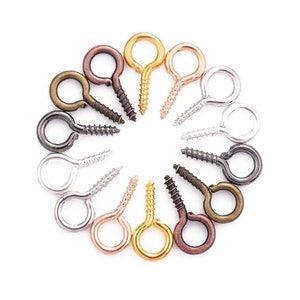 May include: An assortment of screw eye hooks in diverse metallic shades, such as gold, silver, bronze, and copper. The hooks are arranged in a circular pattern against a white backdrop, highlighting their varied colours and textures.