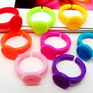 Puede incluir: Conjunto de ocho anillos de plástico de colores con una parte superior redonda y plana. Los anillos son de color rojo, verde, amarillo, naranja, rosa, morado, azul y rosa claro.