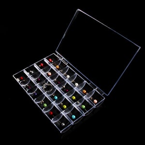 May include: A clear plastic storage box with a hinged lid, containing 24 small compartments. Each compartment holds a single, colorful pearl-like bead.