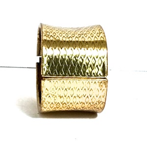May include: A gold-coloured cuff bracelet with a textured diamond pattern. The bracelet is a wide band with a hinged design, and it appears to be made of metal. The bracelet is shown against a white background.