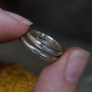May include: Two silver rings with a red stone inlay on each ring.