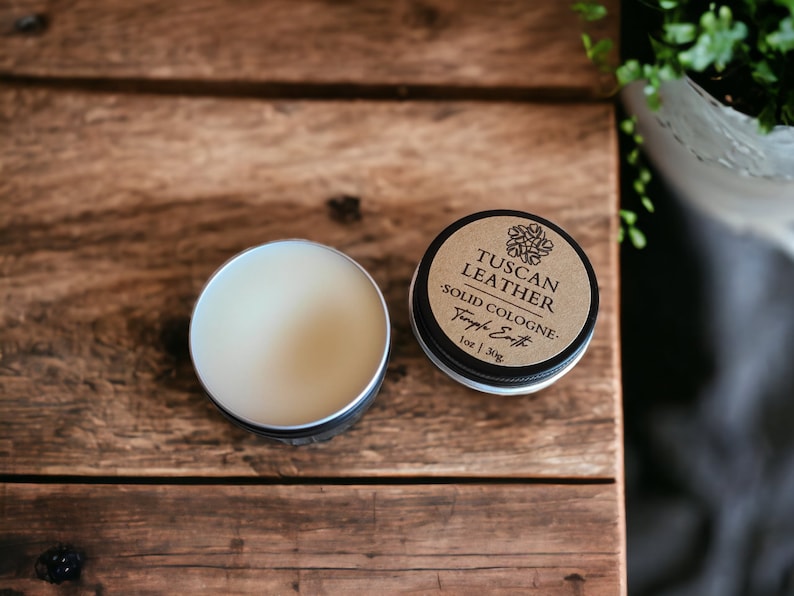Pu&ograve; includere: Un piccolo barattolo rotondo di colonia solida con un'etichetta marrone che recita "Tuscan Leather Solid Cologne - Temple Earth 1 oz | 30g".