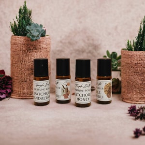 May include: Four small brown glass bottles with roller balls and labels that say "Temple Earth Perfume Roller" and different scents: Patchouli Sandalwood, Patchouli Honey, Vanilla, and Patchouli Ouli.