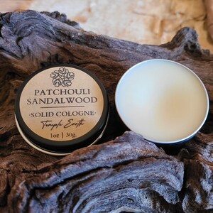 Pu&ograve; includere: Un piccolo barattolo rotondo di colonia solida con un coperchio nero. L'etichetta &egrave; marrone con testo nero che recita "Patchouli Sandalwood - Solid Cologne - Temple Earth 1 oz | 30g". Il barattolo &egrave; aperto e la colonia &egrave; di colore giallo chiaro.