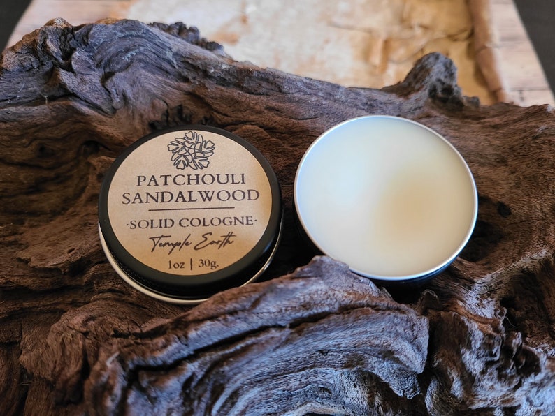Pu&ograve; includere: Un piccolo barattolo rotondo di colonia solida con un coperchio nero. L'etichetta &egrave; marrone con testo nero che recita "Patchouli Sandalwood - Solid Cologne - Temple Earth 1 oz | 30g". Il barattolo &egrave; aperto e la colonia &egrave; di colore giallo chiaro.