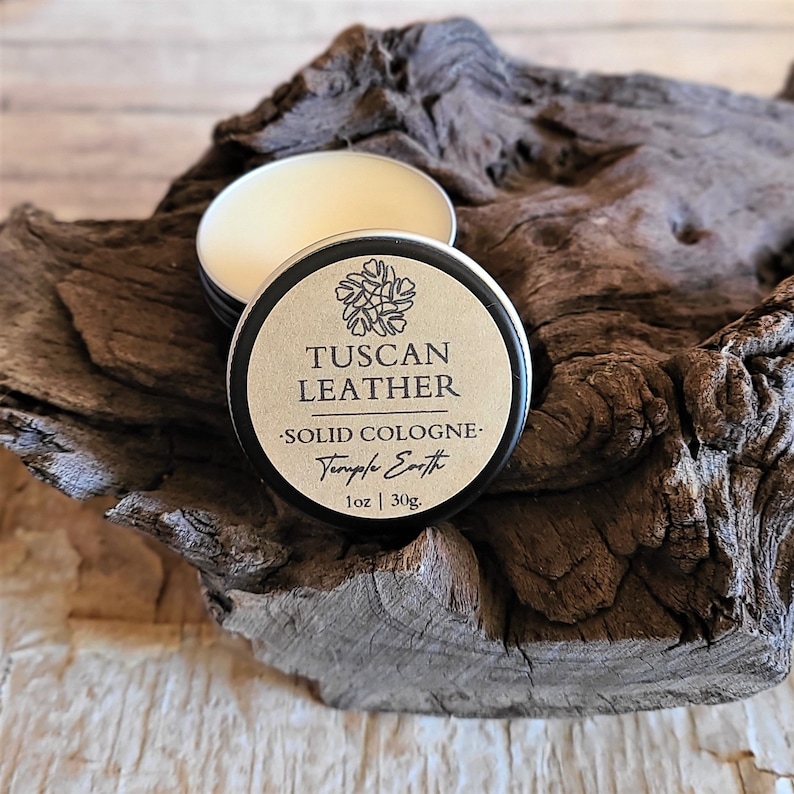 Pu&ograve; includere: Un piccolo barattolo di colonia solida in una scatola di latta marrone e nera con l'etichetta "Tuscan Leather - Solid Cologne - Temple Earth 1 oz | 30g."