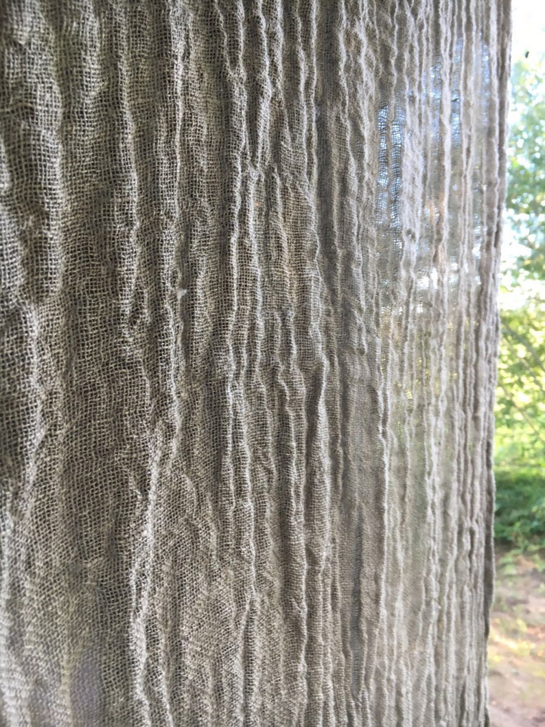 Wrinkled linen curtains hanging by a window. The gauzy linen fabric is very wrinkled in a boho style. Light filters through the gauzy wrinkled fabric.