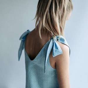 May include: Light blue sleeveless top with white polka dots and tie shoulder straps. The top has a V-neck and is made of a lightweight fabric. The straps are tied into bows. The overall style is casual and feminine.