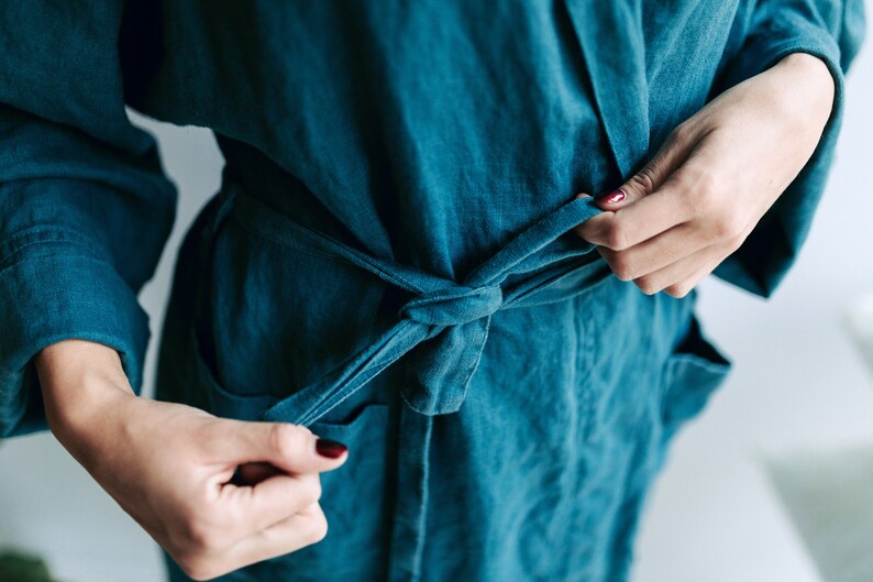 May include: A teal blue robe with a self-tie sash. The robe is made of a soft, textured fabric.