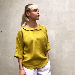 May include: A mustard yellow linen blouse with a peter pan collar and three-quarter sleeves.