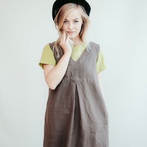 May include: A woman wearing a brown linen dress with a green t-shirt underneath and a black beret.