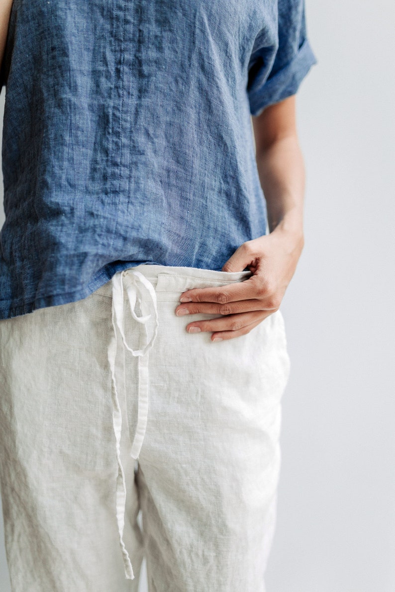 May include: A white linen pants with a drawstring waist and a blue linen shirt.