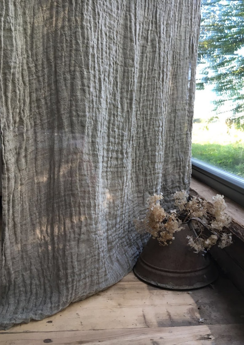 Wrinkled linen curtains hanging by a window, falling effortlessly on a wooden floor. Light filters through the gauzy wrinkled fabric.