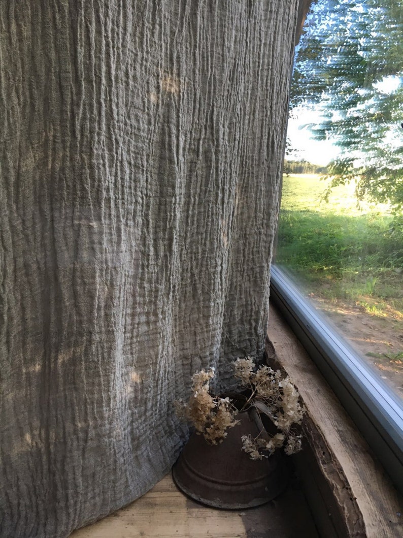 Wrinkled linen curtains hanging by a window, falling effortlessly on a wooden floor. Light filters through the gauzy wrinkled fabric.