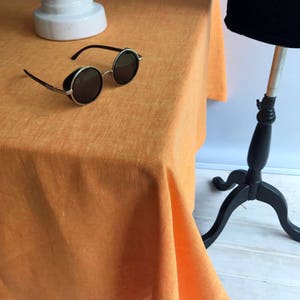 May include: A bright orange linen tablecloth with a slightly textured surface. The tablecloth is draped over a table and hangs down the sides.