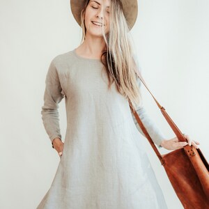 May include: A woman wearing a light gray linen dress with a brown hat and a brown leather shoulder bag.