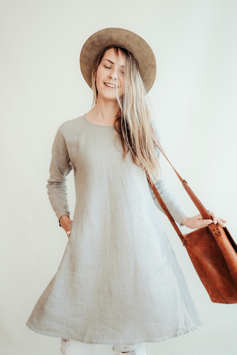 May include: A woman wearing a light gray linen dress with a brown hat and a brown leather shoulder bag.