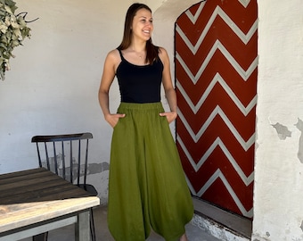 May include: A woman wearing a black tank top and olive green linen pants with a wide leg. She is standing in front of a red door with a white chevron pattern.