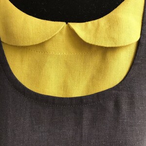 May include: A black linen dress with a yellow Peter Pan collar. The collar is sewn on to the dress and has a rounded shape.