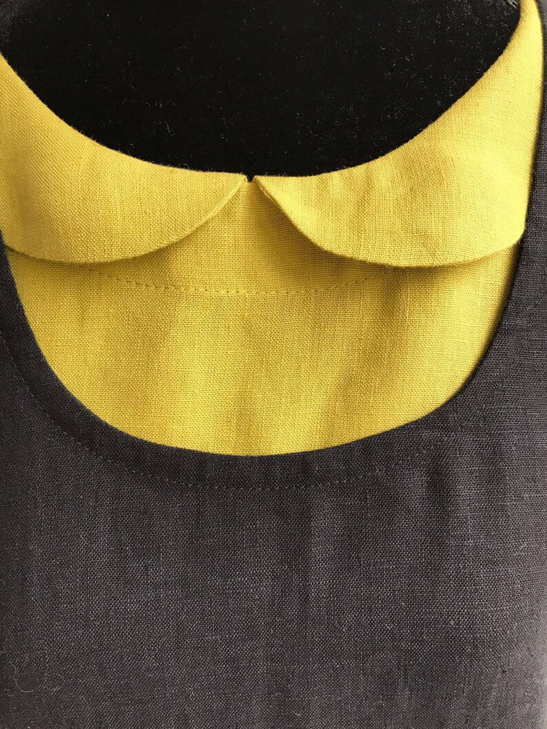 May include: A black linen dress with a yellow Peter Pan collar. The collar is sewn on to the dress and has a rounded shape.