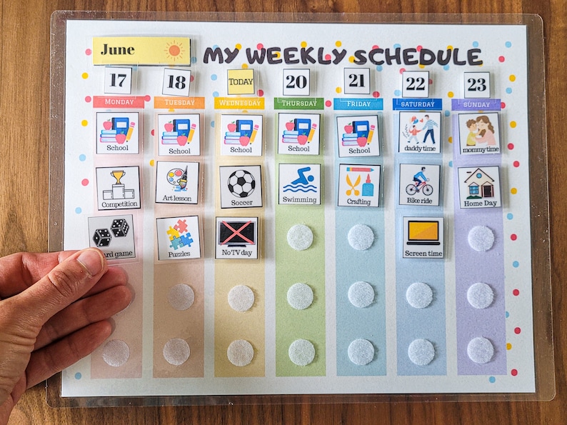 May include: A weekly schedule chart with a clear plastic cover. The chart is divided into seven columns, one for each day of the week. Each column has a number representing the day of the month, the day of the week, and a colour. The chart has a variety of colourful icons representing activities, such as school, art lesson, football, swimming, crafting, bike ride, home day, screen time, and more.