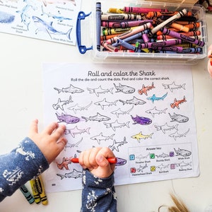 May include: A black and white printable shark activity sheet with a color key. The sheet has a title that says "Roll and color the Shark". The instructions say "Roll the die and count the dots. Find and color the correct shark."