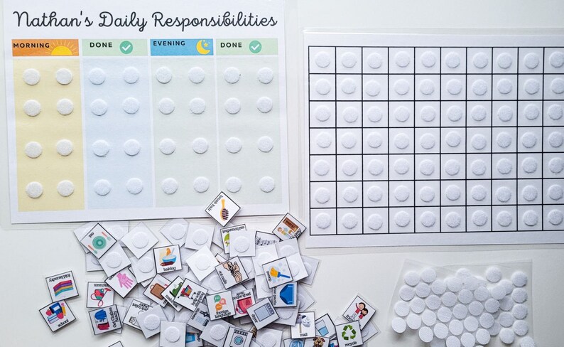 K&ouml;nnte beinhalten: Ein wei&szlig;es Brett mit dem Titel "Nathan's Daily Responsibilities", das in Morgen- und Abendabschnitte unterteilt ist. Jeder Abschnitt hat eine Spalte f&uuml;r Aufgaben und eine Spalte zum Markieren von Aufgaben als erledigt. Auf dem Brett befinden sich wei&szlig;e Kreise zum Anbringen von Aufklebern. Unter dem Brett liegt ein Stapel kleiner quadratischer Aufkleber mit verschiedenen Bildern. Es gibt ein separates Blatt Papier mit einem Raster aus wei&szlig;en Kreisen.