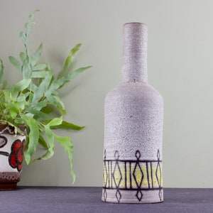 May include: A gray ceramic vase with a yellow and black geometric design around the middle. The vase has a textured surface.