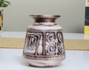 May include: A vintage ceramic vase in brown and white. The vase has a distinctive geometric pattern in a lighter brown shade. It has a broad base and a slender neck, ideal for displaying flowers or as a decorative item. The vase is approximately 15 cm tall.