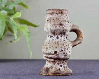 May include: A small, white ceramic vase with a brown glaze and a textured surface. The vase has a rounded body and a single handle.