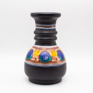 May include: A black ceramic vase with a brown, white, blue, green, and yellow geometric pattern. The vase has a wide base and a narrow neck.