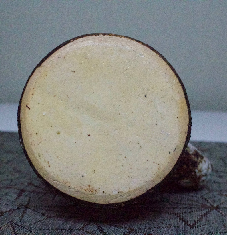 May include: The base of a ceramic mug with a brown rim and a white interior. The mug is glazed and has a smooth finish.