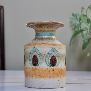 May include: A ceramic vase with a brown, white and blue geometric pattern. The vase has a wide mouth and a narrow base.