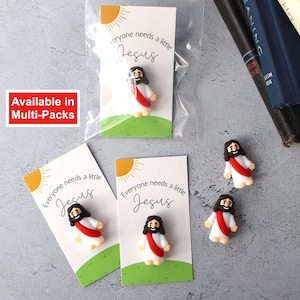May include: Four small, colorful, cartoon-style Jesus figurines with red robes and halos. Each figurine is attached to a white card with the text "Everyone needs a little Jesus".