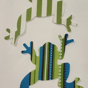 May include: A pack of three frog-shaped fabric appliques. The frogs are green and white striped, green and blue striped, and green and brown striped. The pack is labeled "Pack 3".