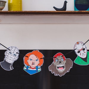 May include: A Halloween banner with black string and colorful paper cutouts of horror movie characters. The characters include Freddy Krueger, Pinhead, Chucky, Jason Voorhees, and a zombie.
