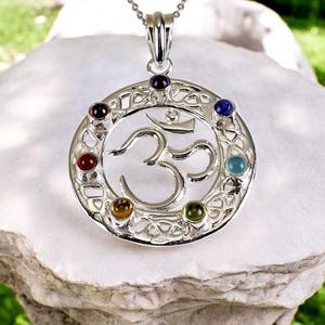 May include: Silver pendant necklace with a detailed Om symbol and seven chakra gemstones. The stones are amethyst, black onyx, red carnelian, yellow citrine, green aventurine, blue turquoise, and lapis lazuli.
