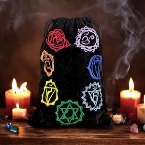 May include: Black velvet pouch with colorful embroidered chakra symbols, including the Om symbol, against a backdrop of lit candles and crystals.