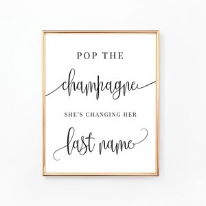 Könnte beinhalten: Gerahmter Druck mit goldenem Rand und weißem Hintergrund. Der schwarze Text lautet „POP THE champagne SHE'S CHANGING HER last name“. Ein dekoratives Schild für eine Brautparty oder Hochzeit.