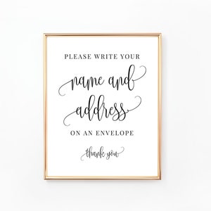May include: A white sign with a gold frame that says "Please write your name and address on an envelope, thank you".