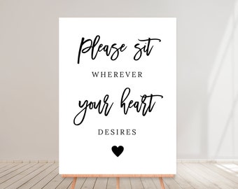 May include: White sign with black text that reads "Please sit wherever your heart desires" with a black heart at the bottom.