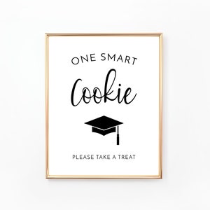May include: A gold framed sign with the text "One Smart Cookie" in black lettering. A black graduation cap icon is below the text. The sign also says "Please Take A Treat" in black lettering.