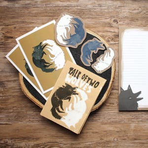 Könnte beinhalten: Ein Schreibwarensortiment mit einem Schwarz-Weiß-Wolf-Design. Das Set enthält ein Notizbuch, zwei Postkarten und drei Aufkleber. Das Notizbuch hat den Text "Tale of Two Wolves" auf dem Cover. Die Aufkleber und Postkarten zeigen ein Schwarz-Weiß-Wolf-Design.