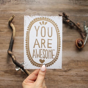 "Handgefertigter Linoldruck ""You Are Super Super"" in Gold auf Weiß - Postkartenformat."