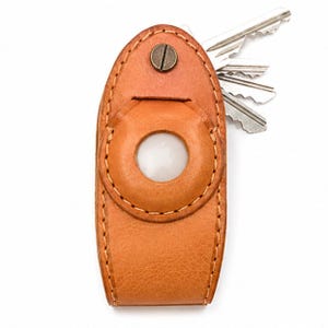 May include: A brown leather key organizer with a circular design and a metal screw closure. Several keys are visible, extending from the side. The key holder is stitched with a contrasting thread, and the leather has a textured appearance.