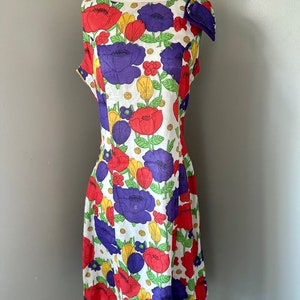 May include: A white sleeveless dress with a floral print featuring red, purple, yellow, and green flowers. The dress has a scoop neck and a fitted bodice.